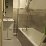 Salle de bain équipée d’une baignoire avec rideau de douche, meuble vasque avec miroir et carrelage beige