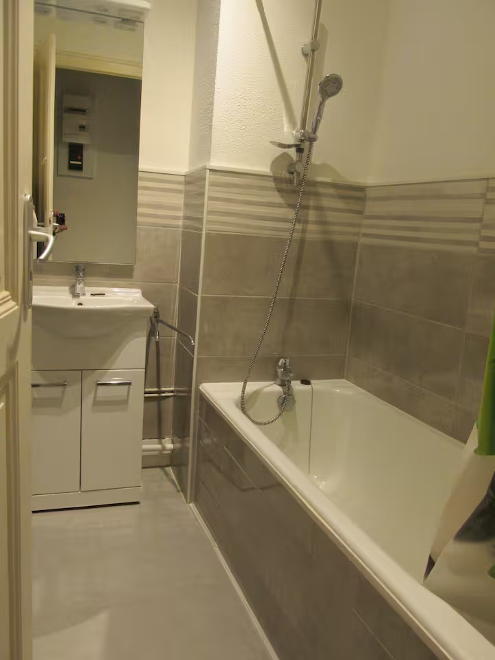 Salle de bain équipée d’une baignoire avec rideau de douche, meuble vasque avec miroir et carrelage beige